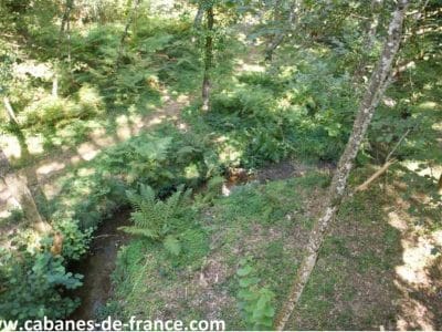 Cabane perchée en Midi-Pyrénées, entourée de verdure et dun ruisseau paisible.
