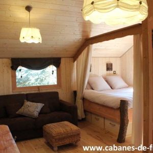 Cabane en bois cosy avec lit douillet et coin salon chaleureux en Auvergne-Rhône-Alpes.