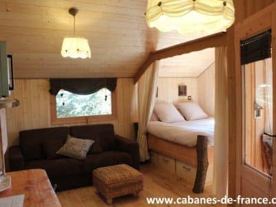 Cabane en bois cosy avec lit douillet et coin salon chaleureux en Auvergne-Rhône-Alpes.