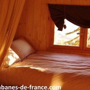 Cabane en bois chaleureuse avec un lit douillet et des fenêtres lumineuses.