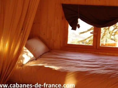 Cabane en bois chaleureuse avec un lit douillet et des fenêtres lumineuses.