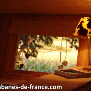 Intérieur dune cabane en bois en Auvergne, avec une lampe décorative et vue sur la nature.