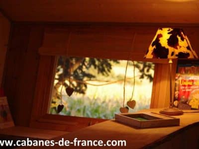 Intérieur dune cabane en bois en Auvergne, avec une lampe décorative et vue sur la nature.