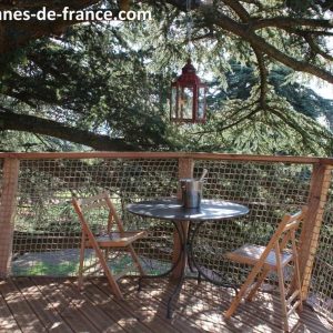 Cabane perchée en Auvergne-Rhône-Alpes avec table et chaises sous un arbre majestueux.