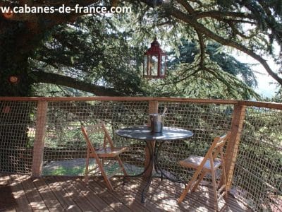 Cabane perchée en Auvergne-Rhône-Alpes avec table et chaises sous un arbre majestueux.