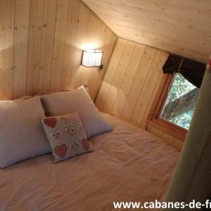 Chalet en bois chaleureux avec lit douillet et éclairage doux, en Auvergne-Rhône-Alpes.