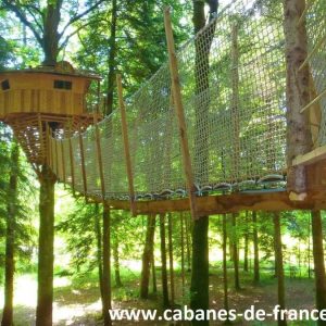 Cabane perchée dans les arbres, accessible par un pont suspendu en bois.