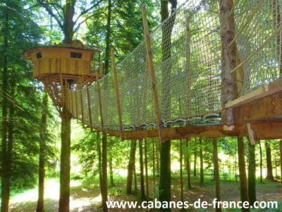 Cabane perchée dans les arbres, accessible par un pont suspendu en bois.