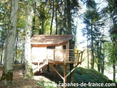 Cabane perchée en bois dans les arbres, entourée de verdure en Bourgogne-Franche-Comté.