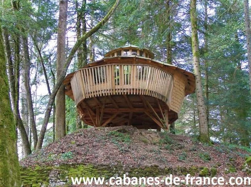 Cabane perchée en bois, entourée darbres, offrant une vue imprenable sur la nature.