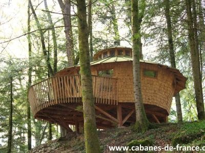 Cabane perchée en bois dans les arbres, entourée de verdure en Bourgogne-Franche-Comté.