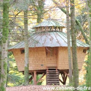 Cabane en bois perchée dans les arbres, entourée de verdure en Bourgogne-Franche-Comté.