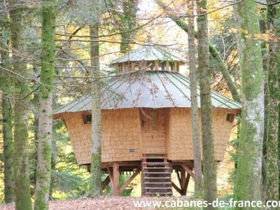 Cabane en bois perchée dans les arbres, entourée de verdure en Bourgogne-Franche-Comté.