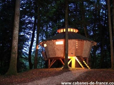 Cabane perchée en bois, illuminée, nichée dans la forêt de Bourgogne-Franche-Comté.