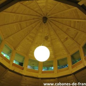 Intérieur dune cabane en bois avec un plafond en forme de dôme et une lumière suspendue.