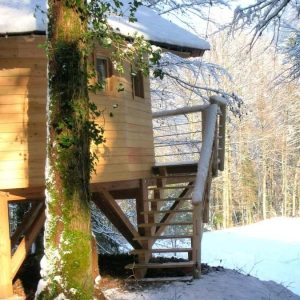 Cabane en bois perchée, entourée de neige et de sapins en Bourgogne-Franche-Comté.