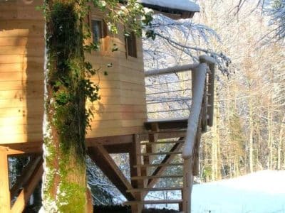 Cabane en bois perchée, entourée de neige et de sapins en Bourgogne-Franche-Comté.