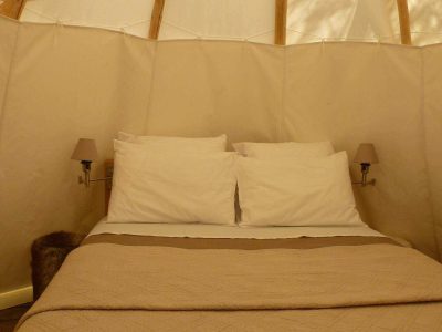 Tente lodge cosy à Limousin, avec lit douillet et lampes murales élégantes.