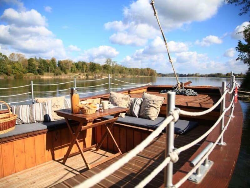 Hébergement insolite : un bateau sur la rivière, avec coussins confortables et vue paisible.
