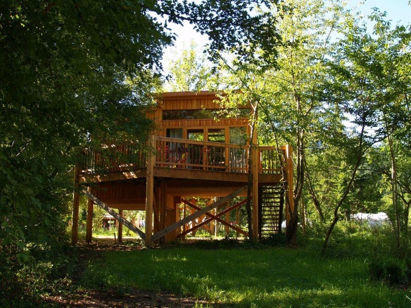 Cabane perchée en bois, entourée darbres verdoyants en Auvergne.
