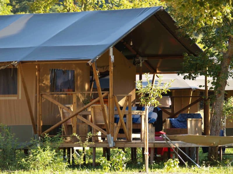 Tente safari en Auvergne, perchée sur pilotis avec terrasse en bois et verdure environnante.