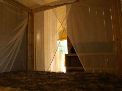Hébergement insolite en Auvergne : cabane en bois avec moustiquaire et vue sur la nature.