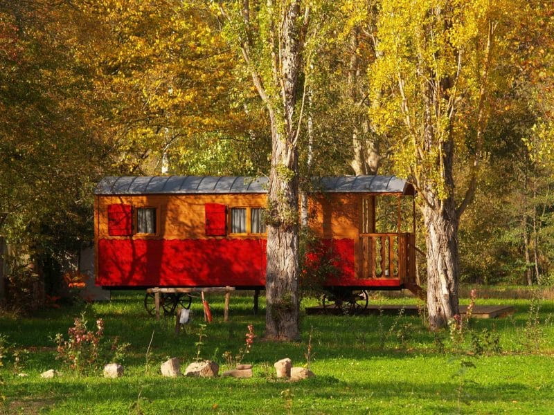 Roulotte colorée nichée entre des arbres aux feuilles dorées en Auvergne.