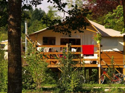 Hébergement insolite en Auvergne : tente lodge sur pilotis avec terrasse en bois.
