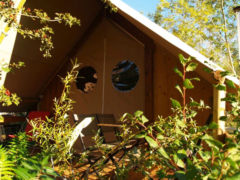 Tente lodge en Auvergne, avec fenêtres rondes et verdure environnante.