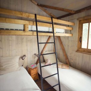 Chalet en bois avec lits superposés et fenêtre lumineuse, idéal pour un séjour en Auvergne.