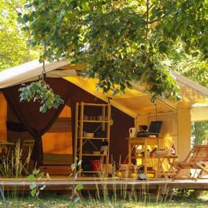 Tente safari spacieuse en Auvergne, entourée darbres verdoyants et mobilier coloré.