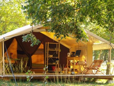 Tente safari spacieuse en Auvergne, entourée darbres verdoyants et mobilier coloré.