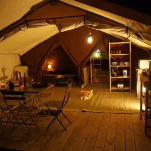 Tente safari spacieuse en Auvergne, avec éclairage doux et mobilier en bois.
