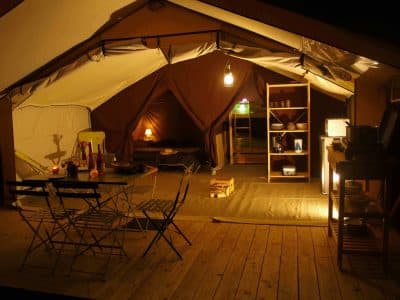 Tente safari spacieuse en Auvergne, avec éclairage doux et mobilier en bois.
