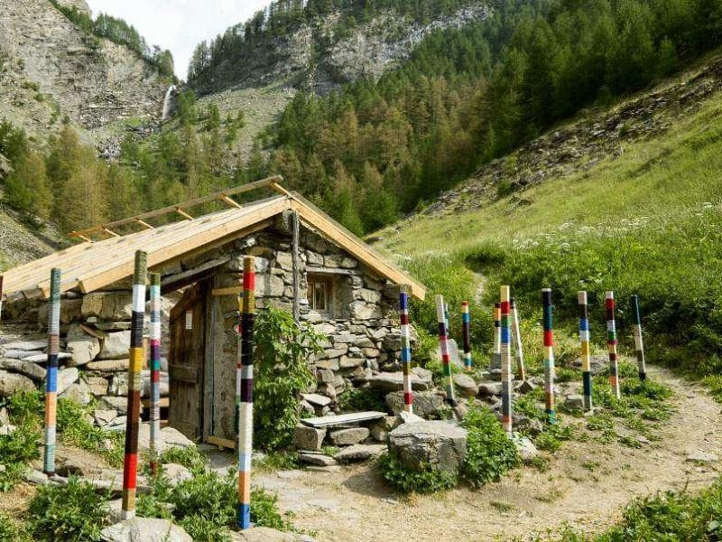 Cabane en pierre entourée de poteaux colorés, nichée dans la vallée alpine.