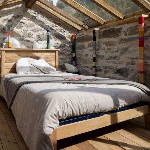 Chalet en bois avec murs en pierre et lit douillet sous un toit vitré.