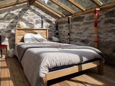 Chalet en bois avec murs en pierre et lit douillet sous un toit vitré.