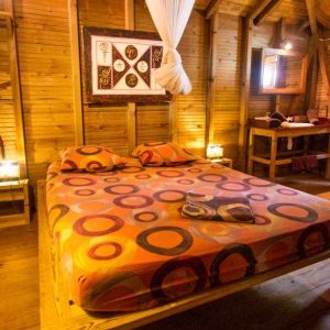 Chalet en bois avec lit coloré et décoration chaleureuse, ambiance tropicale.