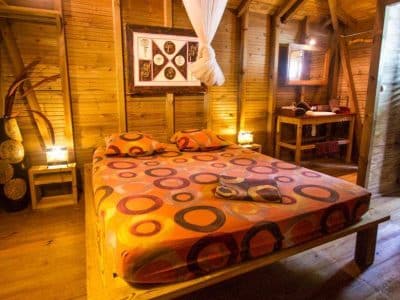Chalet en bois avec lit coloré et décoration chaleureuse, ambiance tropicale.