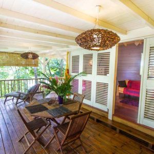 Cabane en bois avec terrasse, décorée de luminaires en osier et verdure environnante.