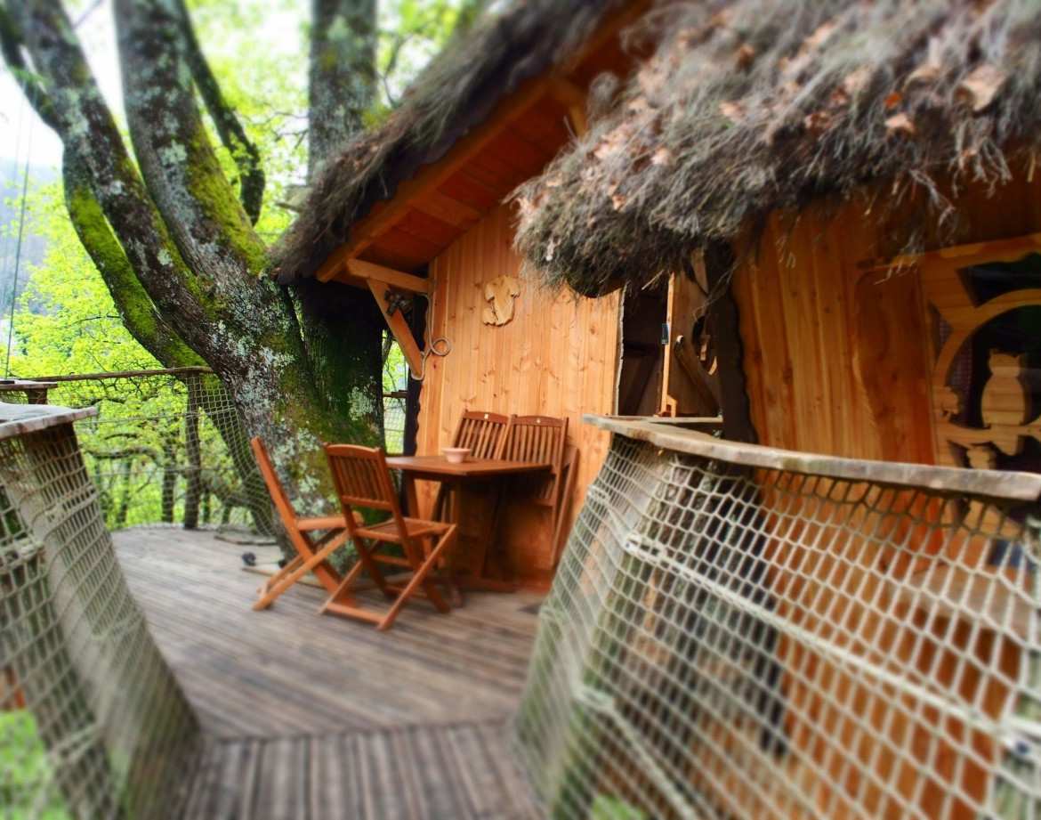 Cabane perchée en bois avec terrasse en bois, entourée darbres verdoyants.