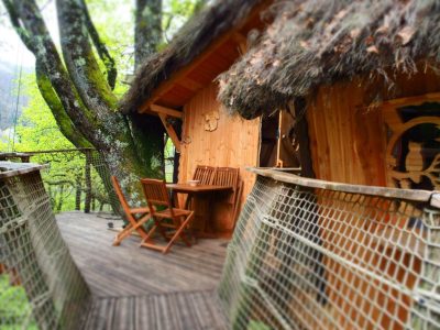Cabane perchée en bois avec terrasse en bois, entourée darbres verdoyants.