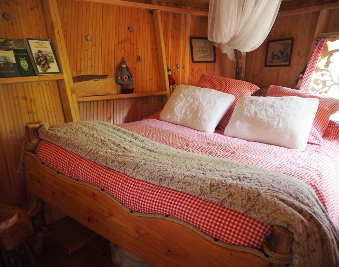 Cabane en bois avec lit douillet, draps à carreaux rouges et ambiance chaleureuse.