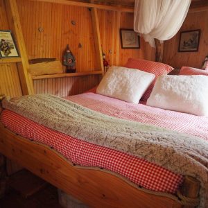Cabane en bois avec lit douillet, draps à carreaux rouges et ambiance chaleureuse.