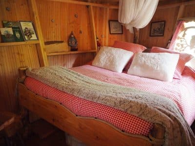 Cabane en bois avec lit douillet, draps à carreaux rouges et ambiance chaleureuse.