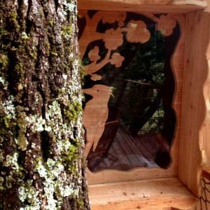 Cabane perchée en bois avec fenêtre sculptée, nichée dans un arbre en Auvergne.