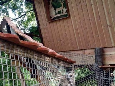 Cabane perchée en bois avec un décor naturel et un filet de sécurité.