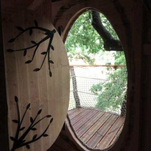 Cabane perchée en bois avec une grande fenêtre ovale offrant une vue sur la nature.