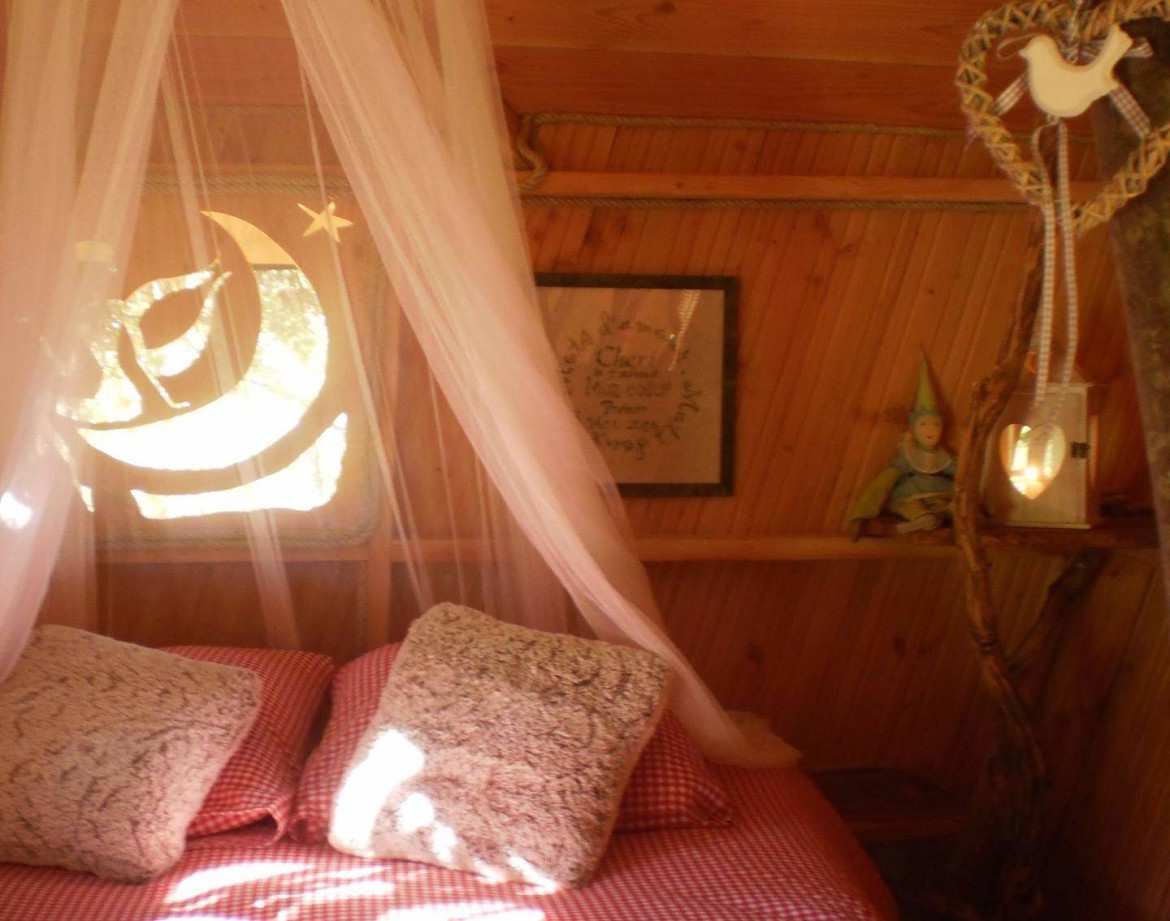 Cabane en bois cosy avec lit douillet, décorée de voilages et déléments naturels.