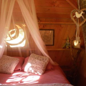 Cabane en bois cosy avec lit douillet, décorée de voilages et déléments naturels.